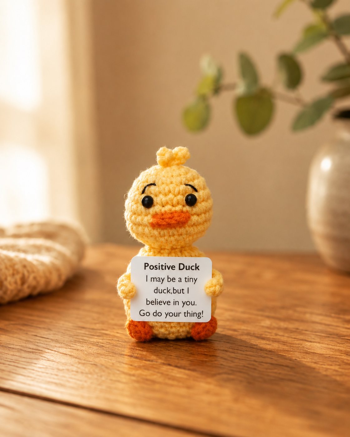 Tiny yellow crochet duck holding a small affirmation card